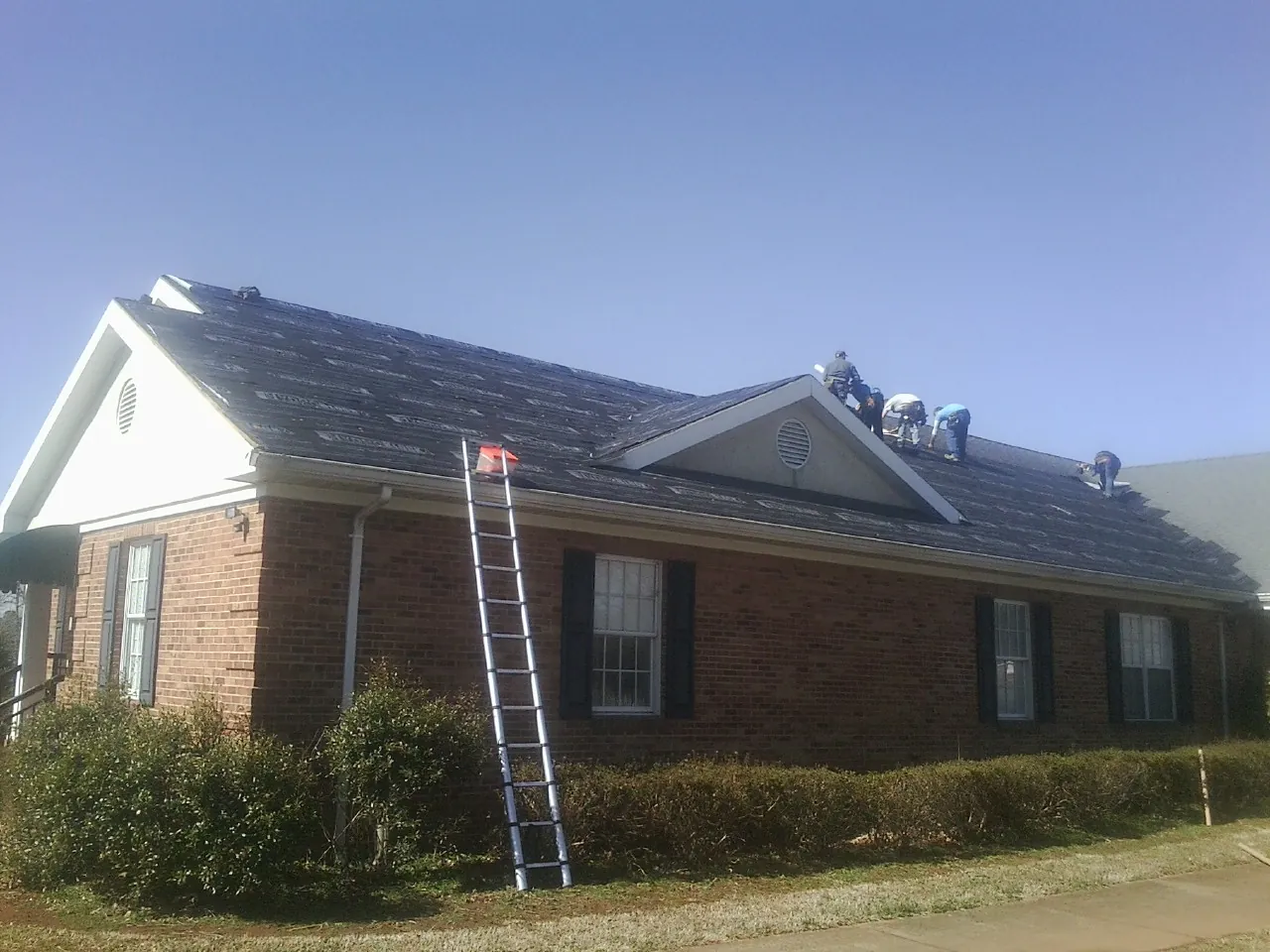 Crew tearing shingles off a brick ranch roof with a ladder set — Metal Roof Repair work by our crew in Marriottsville