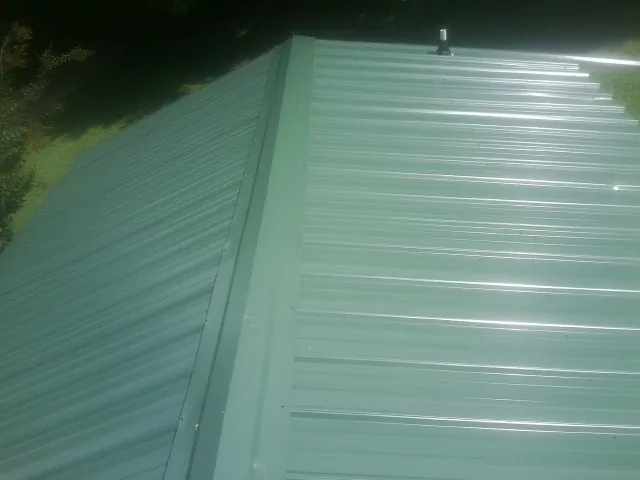 New green metal panels meeting at the ridge of a roof — Flat Roof Repair work by our crew in Marriottsville