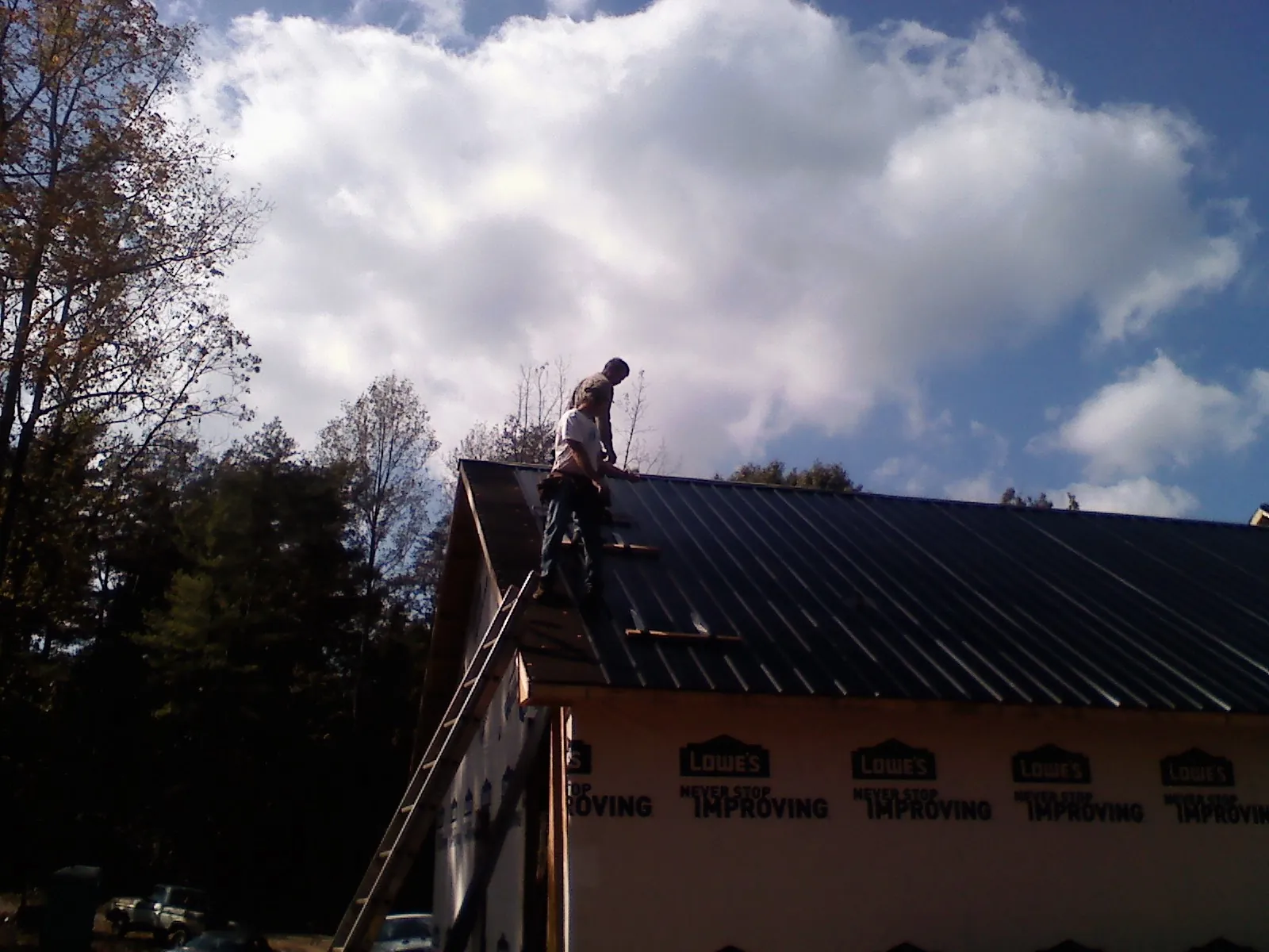 Roofer fastening dark metal panels high against a cloudy sky, from a Roof Inspection job in Marriottsville