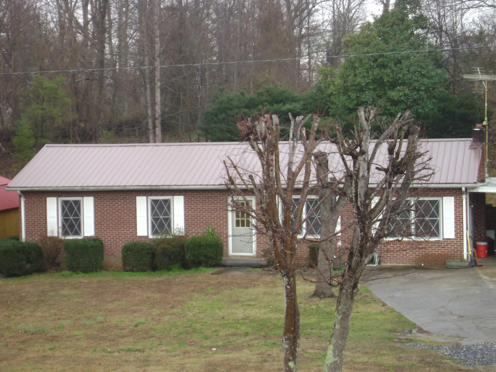 Mauve metal roof on a brick ranch home behind bare trees in Marriottsville