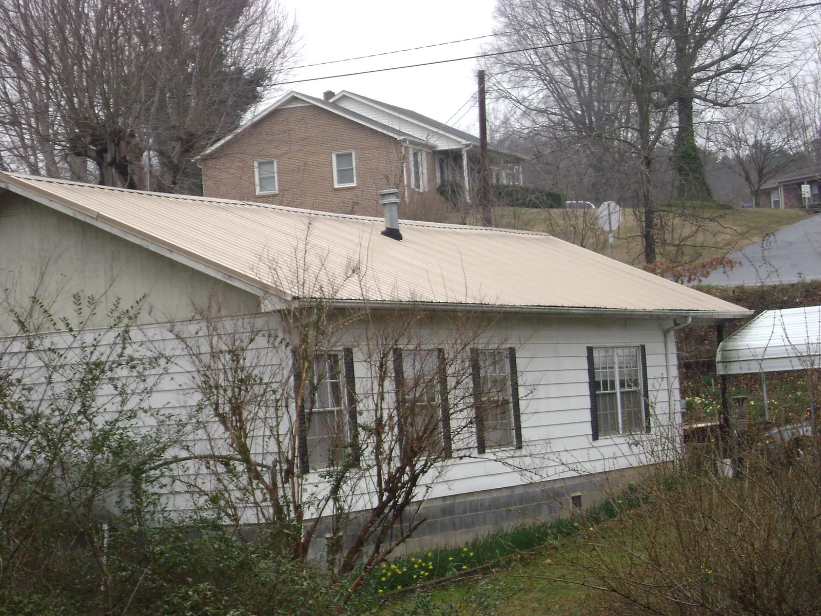 Tan metal roof on a white sided house set into a hillside — Commercial Roofing by Roofing Brothers in Marriottsville